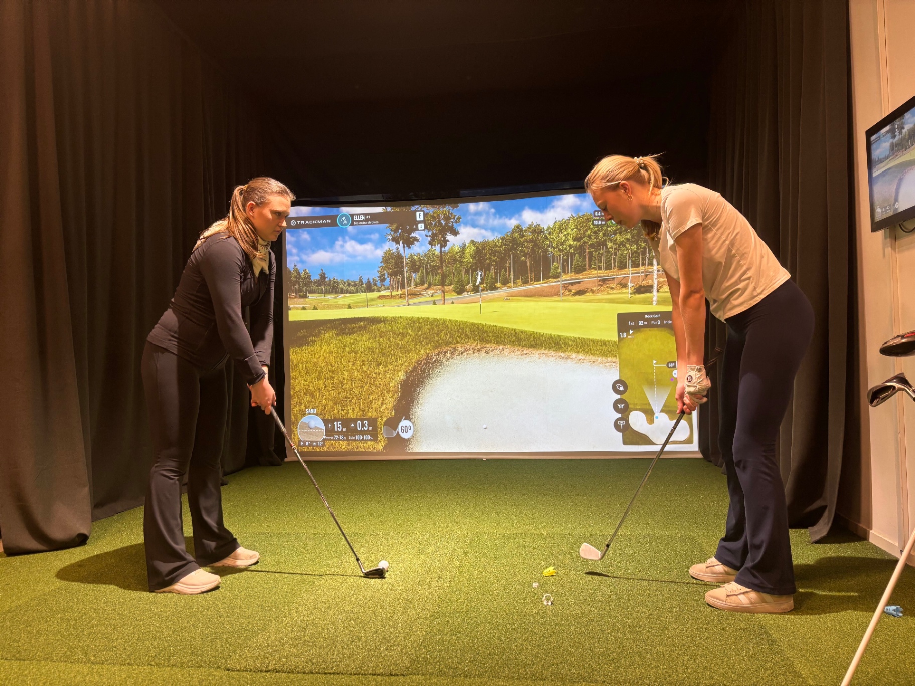 Two golfers practicing at an indoor TrackMan simulator